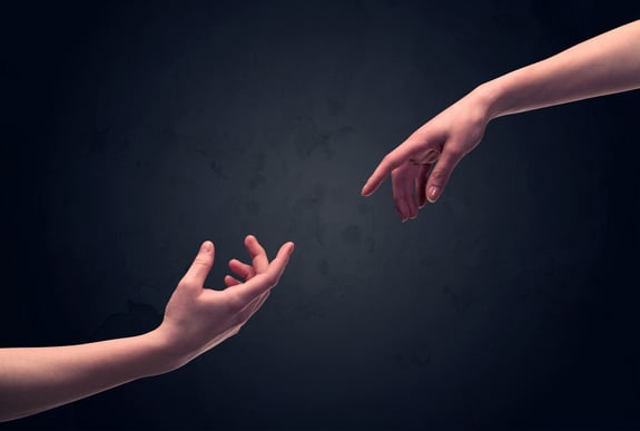Two male hands reaching out to one another, almost touching, in front of dark clear empty background wall concept